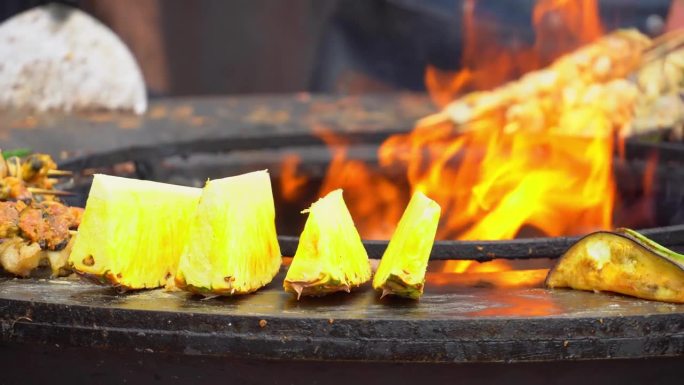 在街头美食节上，肉、蔬菜和海鲜在火上煮熟。厨师用夹子把肉在烤架上翻动。烧烤