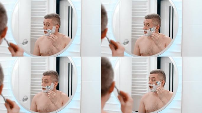 剃刀剃男人的脸。白人男子用剃须刀刮脸。剪掉脸上的胡茬。没刮胡子的男人在剪胡子
