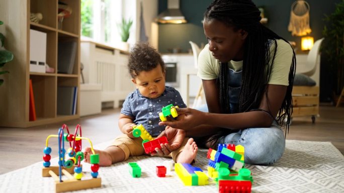 母亲和她的小黑人儿子在家里玩积木玩具