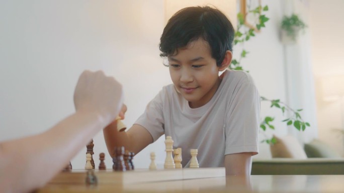 周末，一个亚洲男孩和他爸爸在家里下棋，玩得很开心。