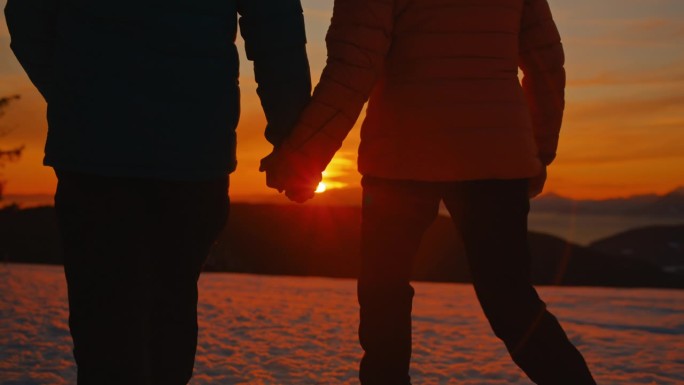 一对无法辨认的老年夫妇在黄金时间牵着手走在雪地里