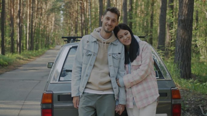 一对幸福的夫妇站在森林里，旁边是汽车，他们从农村的公路旅行中放松下来