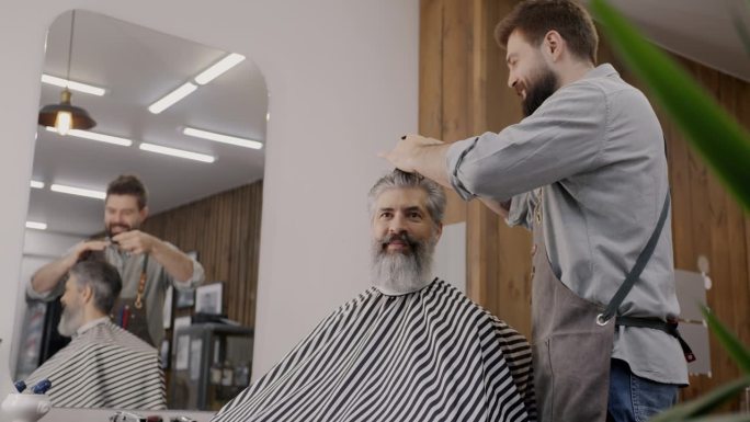 快乐的理发师系着围裙给男人剪头发，在理发店里有说有笑