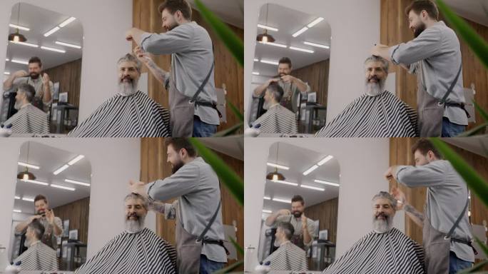 快乐的理发师系着围裙给男人剪头发，在理发店里有说有笑
