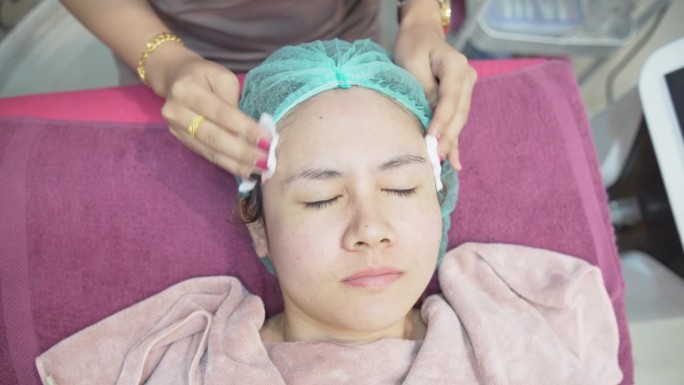 一名护士正在擦拭一名亚洲妇女的脸。在美容诊所，医疗和美容皮肤科预约概念。
