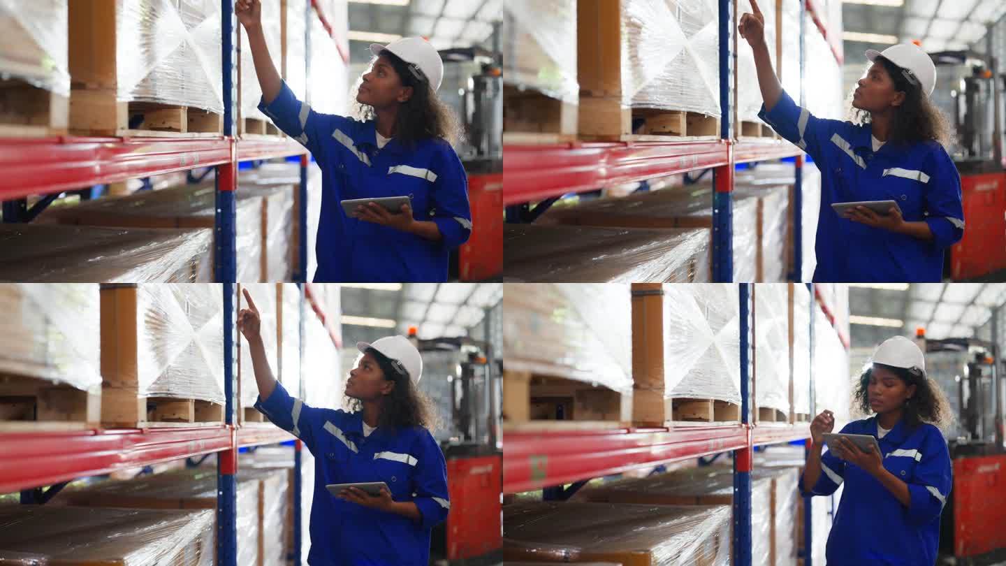 年轻的黑人女仓库工人手持数码平板电脑检查库存管理包装盒。身穿背心、头戴安全帽的非洲裔女工作人员在仓库