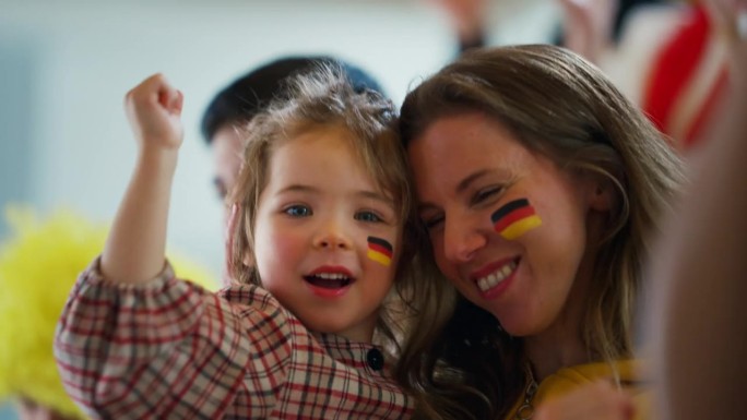 兴奋的足球迷，母亲带着小女儿，在体育场支持德国国家队的实况足球比赛。