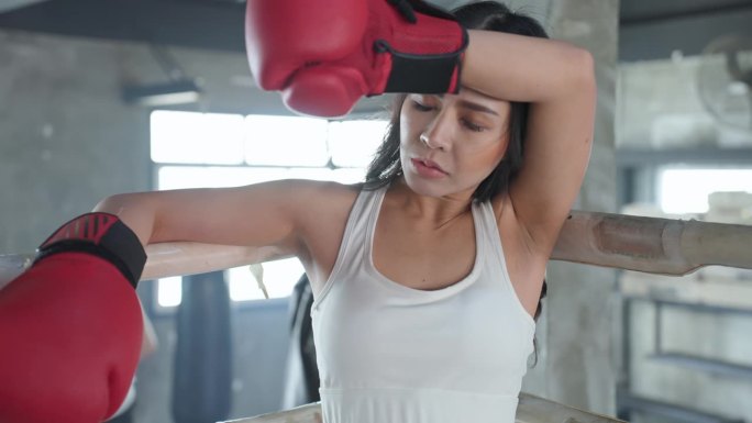在拳击台上进行拳击和搏击。一位亚洲年轻美女在拳击馆的角落里练习拳击，并在用力击打后休息。亚洲女运动员