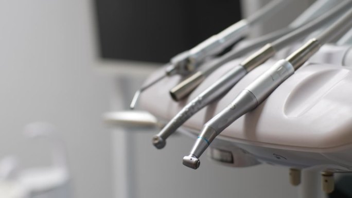 戴着橡胶手套、无法辨认的牙医的手从一套牙科工具中取出电钻，为牙痛患者治疗