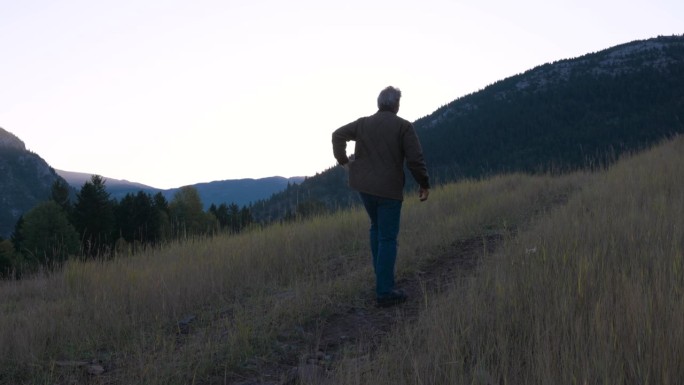 日出时，一个成熟的男人在长满草的小路上穿过草地