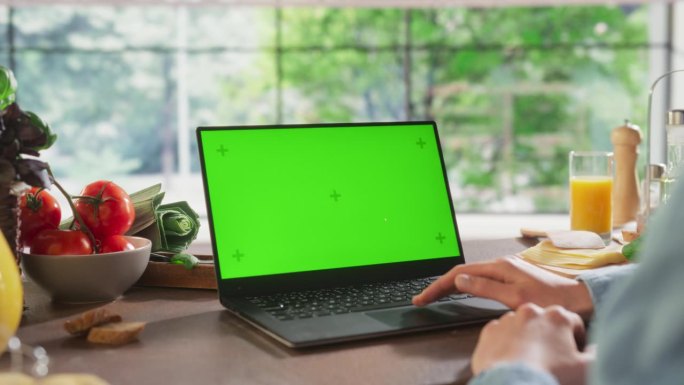 匿名妇女在她的厨房使用笔记本电脑模拟绿屏Chromakey显示与运动跟踪占位符。视频模板内容促进健康