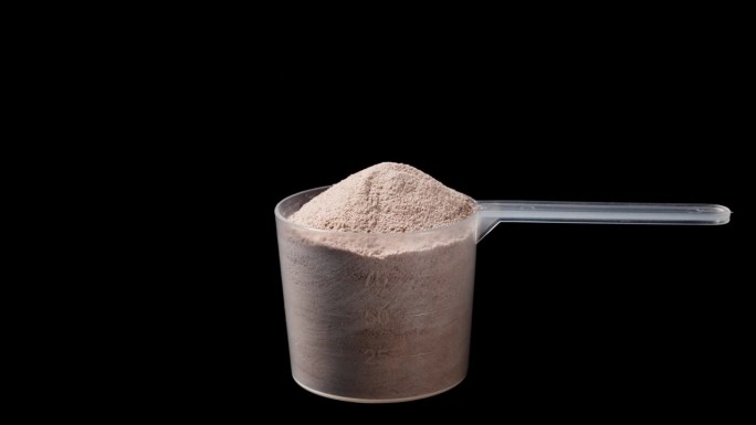 透明测量勺与巧克力蛋白粉，旋转在黑色背景。