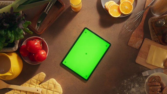 平板电脑的静态视图与模拟绿屏显示。数字设备模板躺在木制的厨房桌子上，周围是健康的食物和新鲜的食材