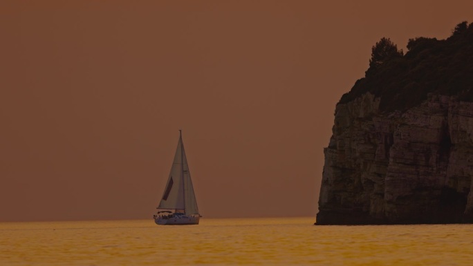 帆船在海洋中航行，夕阳映衬着橙色的天空