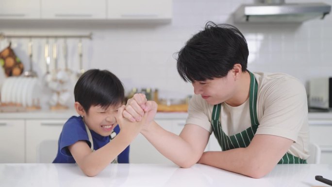 幸福的亚洲家庭概念。父子俩在家里玩扳手腕，一起享受时光。小儿子是冠军