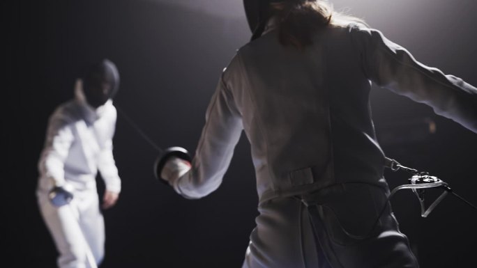 后视图两名职业击剑运动员在比赛中全副防护装备碰撞花剑