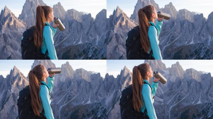女人在山顶喝水，欣赏着周围令人惊叹的景色
