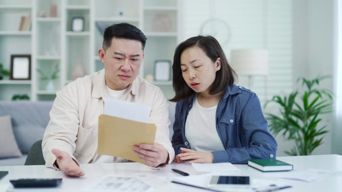 失望的亚洲夫妇坐在家里读坏消息的信