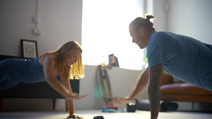 慢动作健身年轻夫妇做击掌俯卧撑，一起在家里阳光明媚的客厅地板上锻炼。健康的生活方式、运动、健身、力量