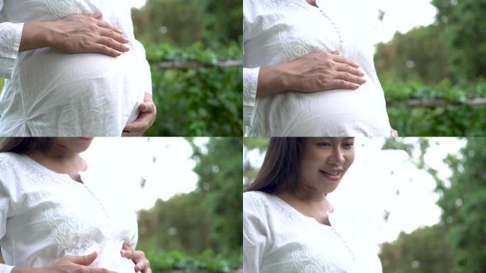 公园里身穿白衣的孕妇双手放在肚子上。怀孕，生育，准备和期望的概念。