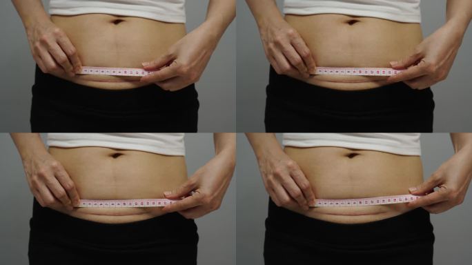 一名妇女正在用卷尺测量腹部剖宫产后的疤痕