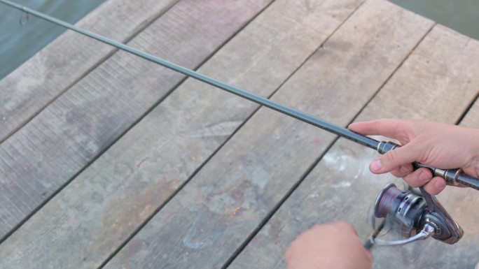 渔夫手里拿着一根鱼竿，站在木码头上转动卷轴。在河里或池塘里打鱼。垂钓者手里拿着一根旋转杆，手里拿着一