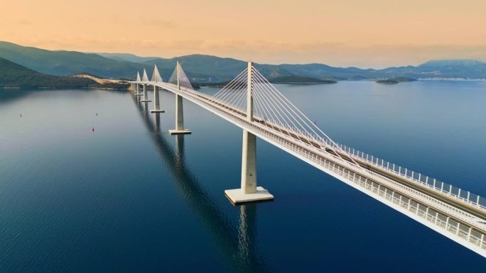 日落时分，佩列沙茨桥在克罗地亚亚得里亚海上空的航拍照片。汽车正在过桥