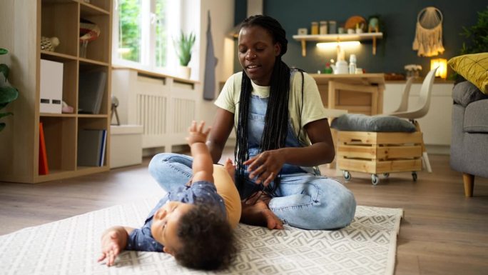 快乐的母亲和婴儿黑人在家里玩耍