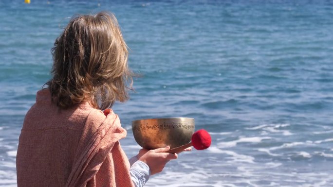 年轻女子在特内里费岛的海边，拿着一只来自尼泊尔的铜唱碗冥想