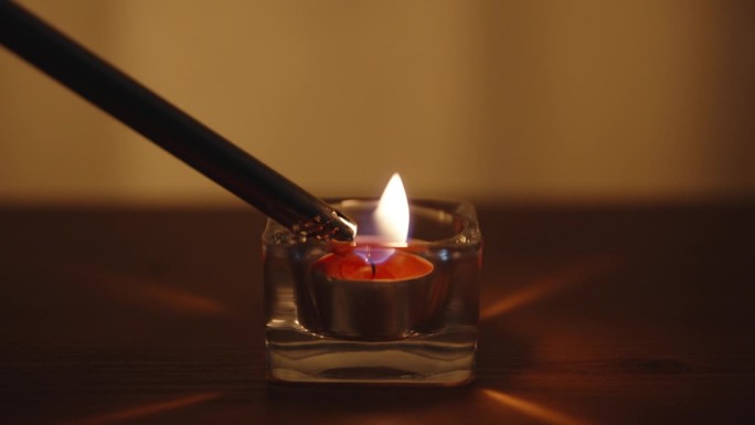 玻璃杯里的红烛。用长打火机点燃。在一张木桌上。