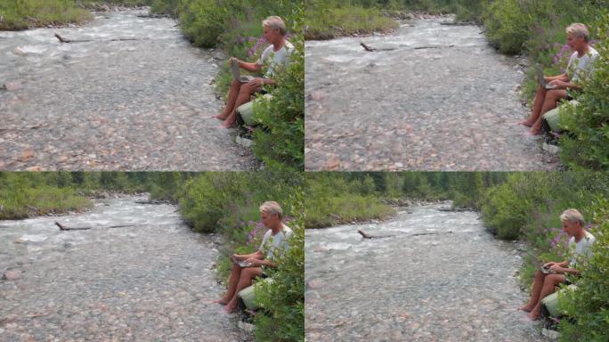 老人在河边休息时使用笔记本电脑