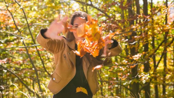 享受秋天的女人，把五彩缤纷的树叶扔向镜头