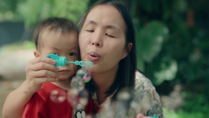 顽皮的亚洲男孩和妈妈在阳光公园享受泡泡游戏-家庭纽带和快乐时刻