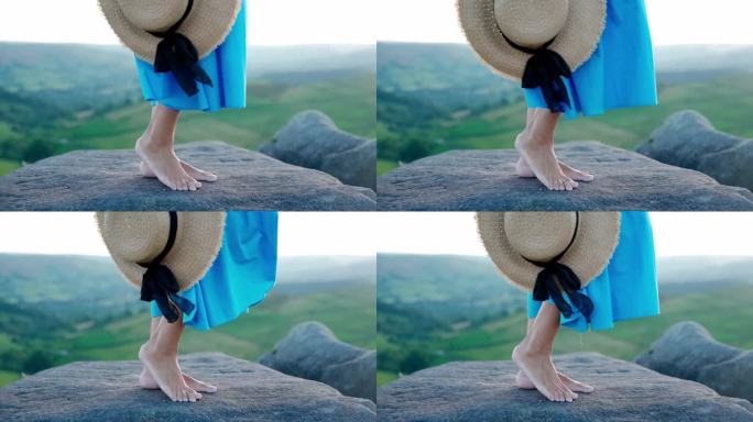 一名亚洲女子身穿蓝色连衣裙，戴着一顶帽子，手里拿着薰衣草花束，站在夏日日落的山顶上