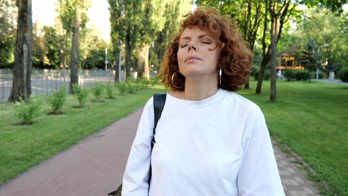 一个30岁的红发女人的肖像，穿着白色的t恤，晚上在公园的路上走着。路边一个女人拿着包的慢动作肖像