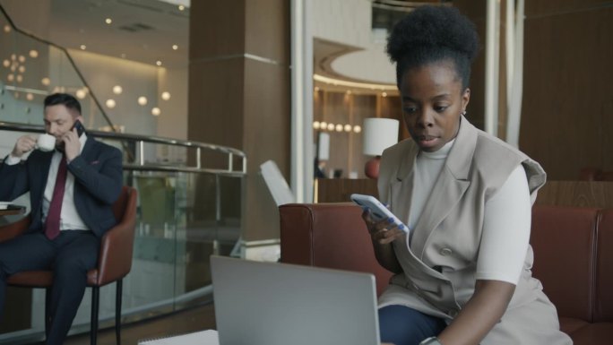 非裔美国女商人在酒店休息室使用笔记本电脑和智能手机
