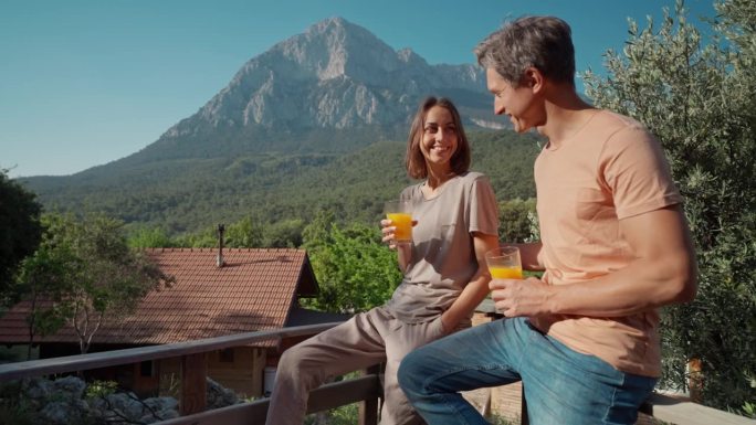 在阳光明媚的早晨，一对快乐的夫妇在户外露营，享受日出，喝着新鲜的橙汁。旅游养生，健康营养理念。