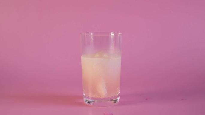 泡腾型维生素C片溶于水。一杯水，粉红色背景的水果味泡沫片。维生素C概念