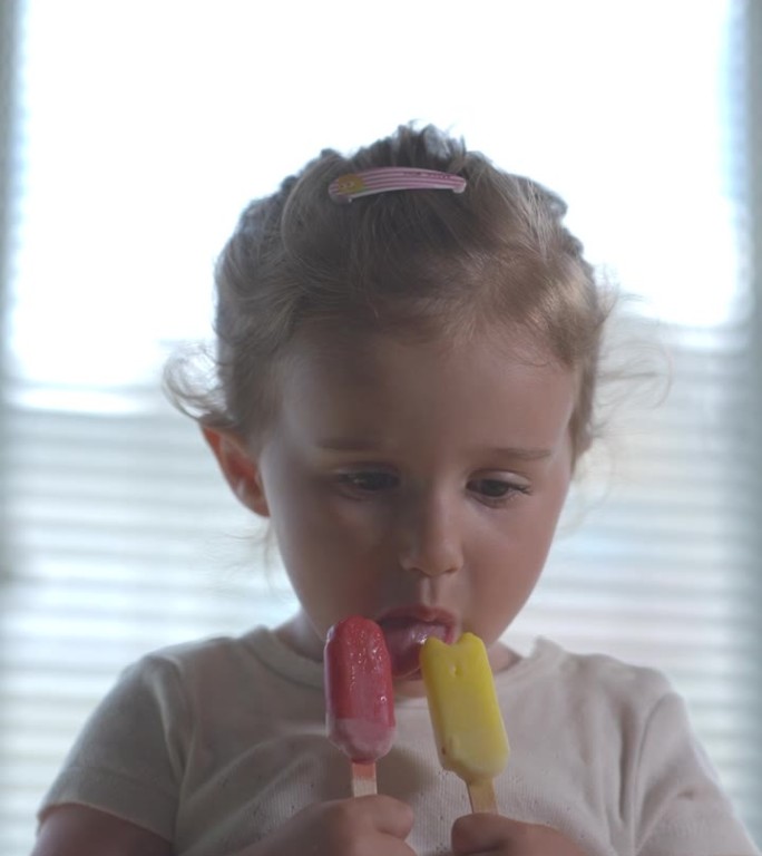 女孩吃着红色和黄色的冰淇淋。