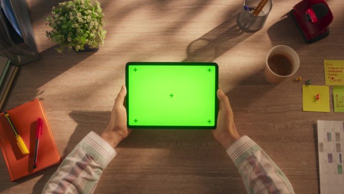 办公室经理拿着绿屏模拟显示屏的平板电脑，坐在创意机构的木桌后面。视频模板的数字演示，通信材料