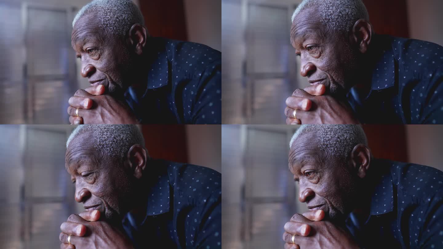 一个沉思的巴西黑人老人的特写脸，双手放在下巴上，表情若有所思。老年人在老年时反思过去的经历