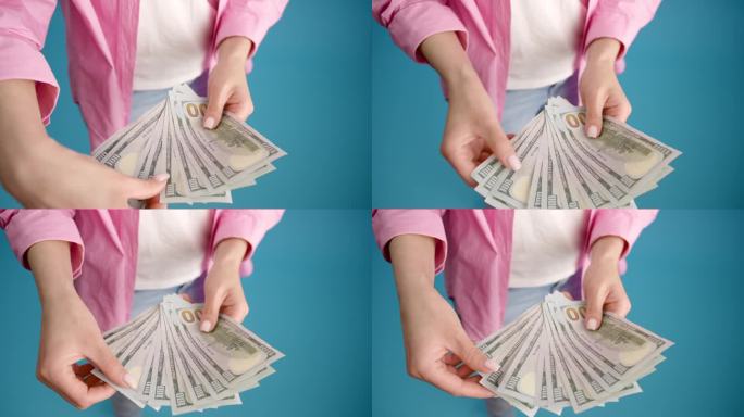 女性手数一叠百元美钞的特写。一位女商人正在数钱。投资、金钱交换、贿赂或腐败的概念。蓝色背景