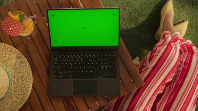 俯视视图的匿名女性坐在花园的桌子上，使用电脑模拟绿屏Chromakey显示与运动跟踪占位符。享受暑假