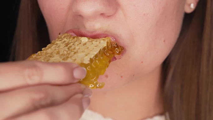 女人吃蜂蜜用蜡蜂房。特写的嘴。健康食品，天然甜食