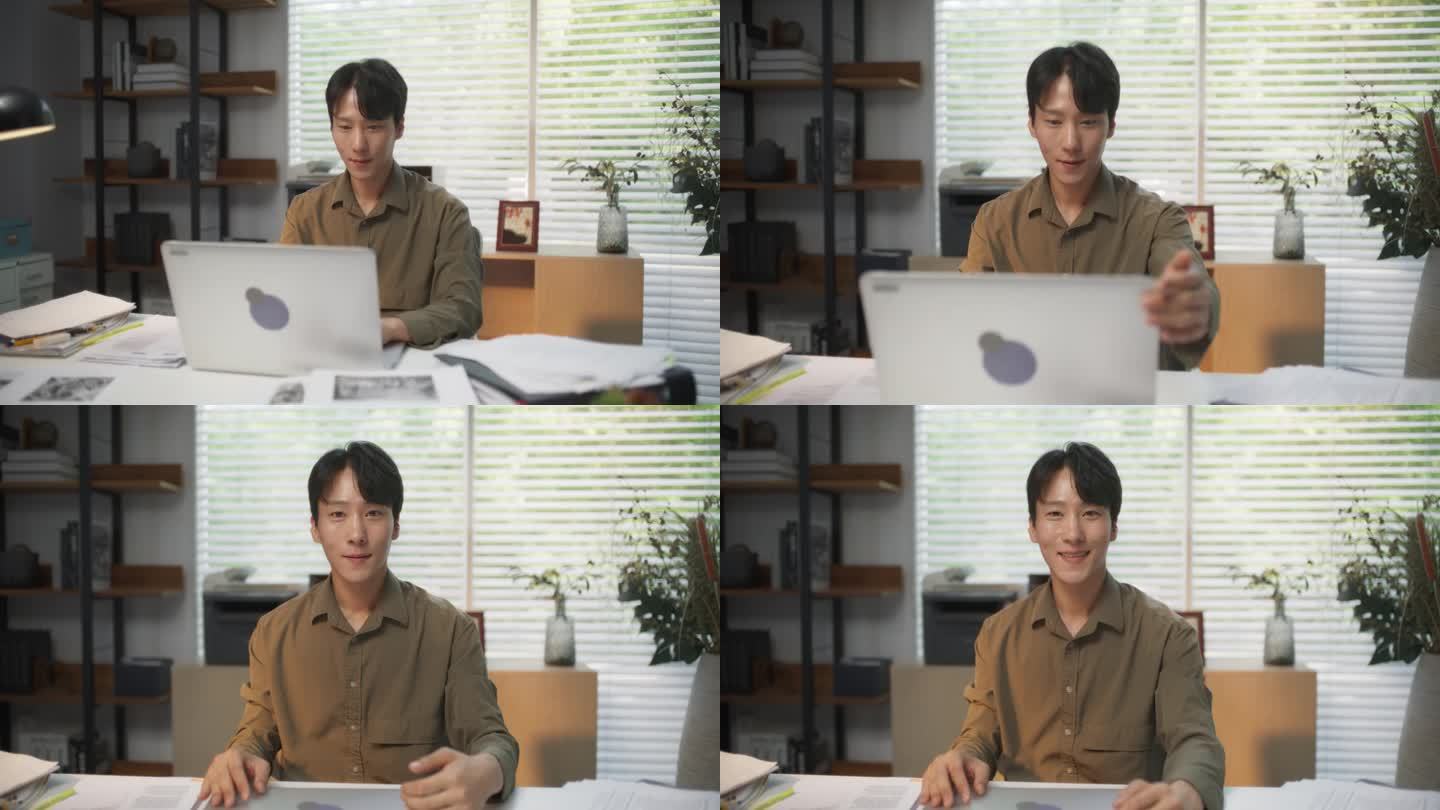 一个帅气的韩国男性在一家时尚创意机构的办公桌后对着电脑工作。快乐的年轻人合上他的笔记本电脑，摆姿势，