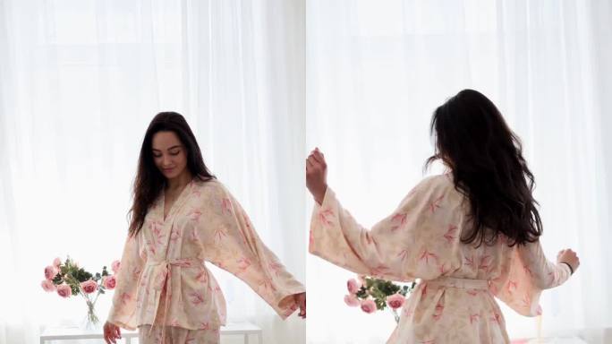 年轻快乐的黑发女人穿着睡衣在房间的花束中跳舞。