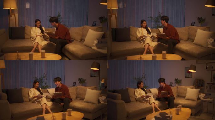 一对韩国夫妇坐在舒适的现代沙发上。年轻英俊的男子用平板电脑看新闻，而他美丽的女友正在看最新一期的时尚