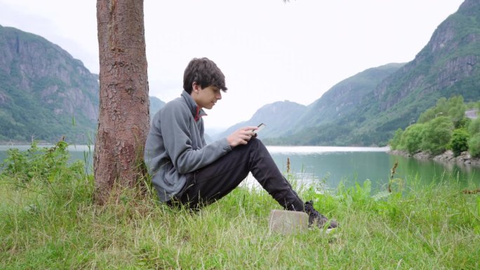 视频4k PRORES HQ。在夏日的绿色森林里，一个年轻的白人孩子躺在露营帐篷附近的草地上，用他的