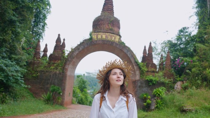 戴草帽的妇女走在通往泰国丛林中一座古庙的大门附近