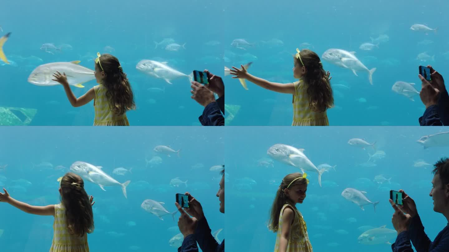 爸爸用智能手机给女儿拍照，小女孩喜欢和爸爸在社交媒体上分享海洋馆的乐趣